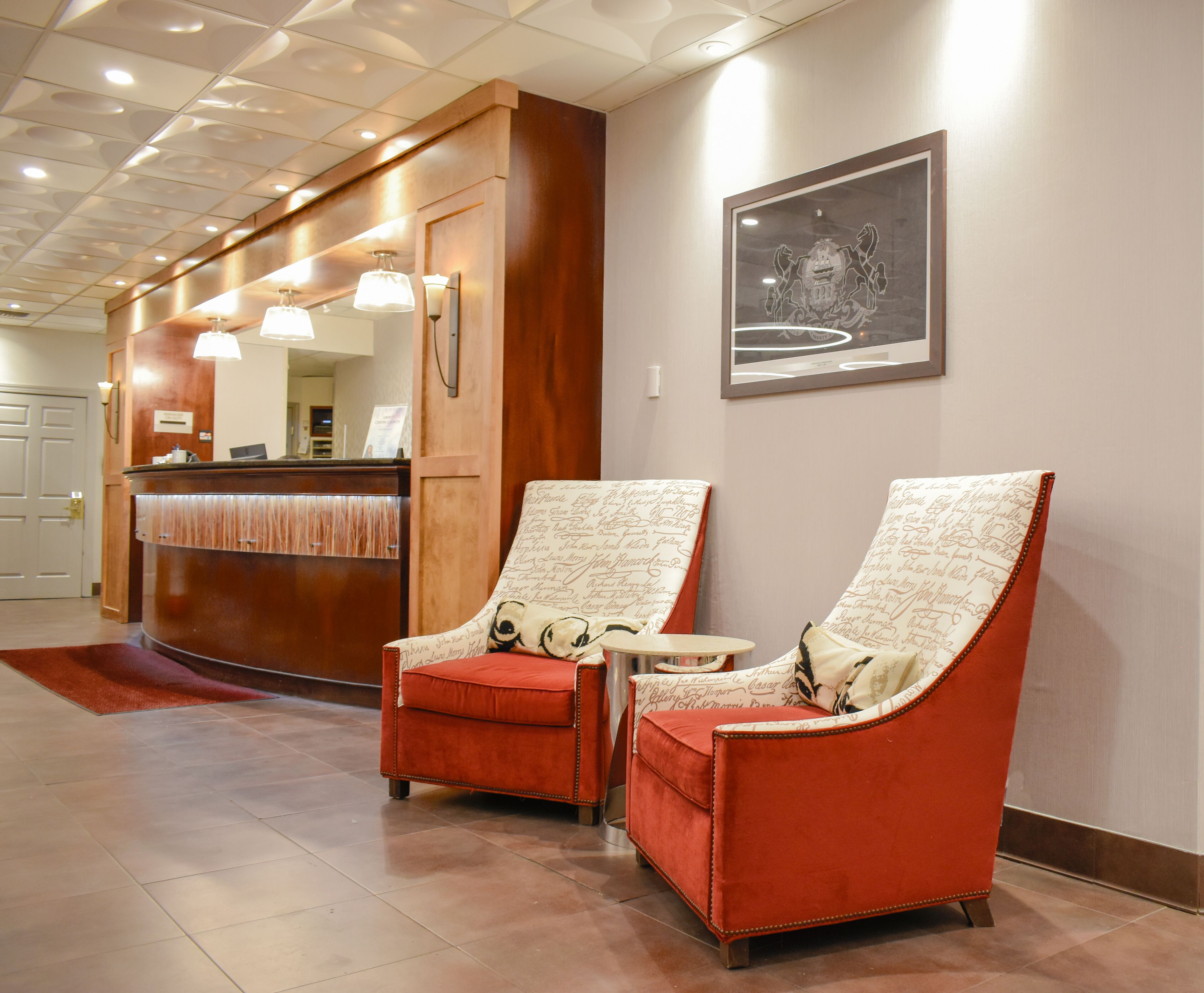 A lobby with two red armchairs, a reception desk, and a framed emblem on the wall.