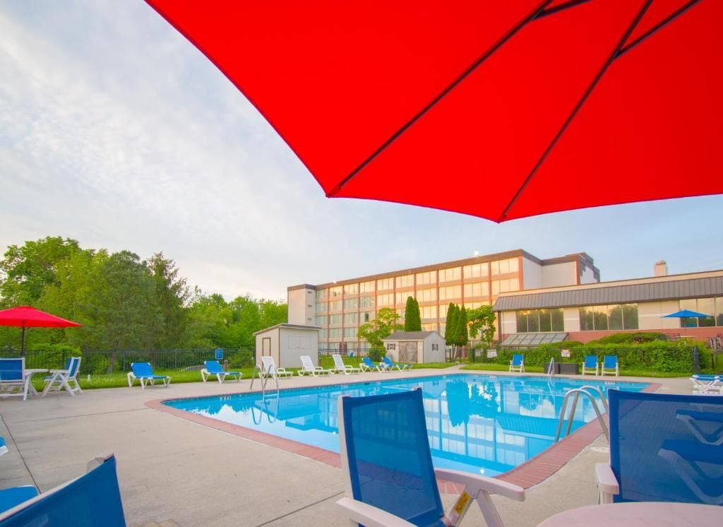 A swimming pool with lounge chairs and umbrellas, surrounded by a building with large windows.