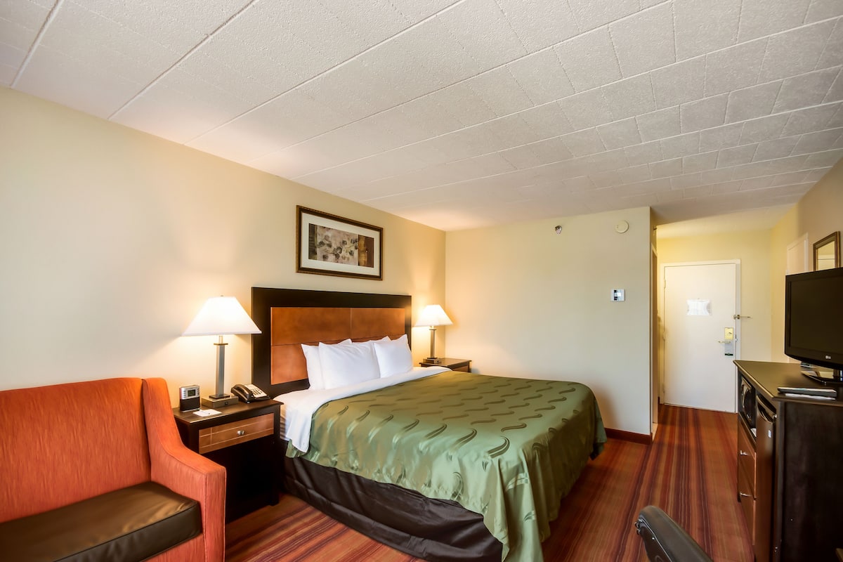 A hotel room with a bed, two bedside lamps, a desk with a telephone, a television, and a chair.