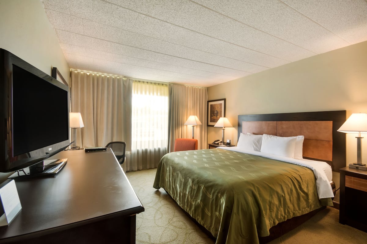 A hotel room with a bed, a desk with a TV, and two lamps.