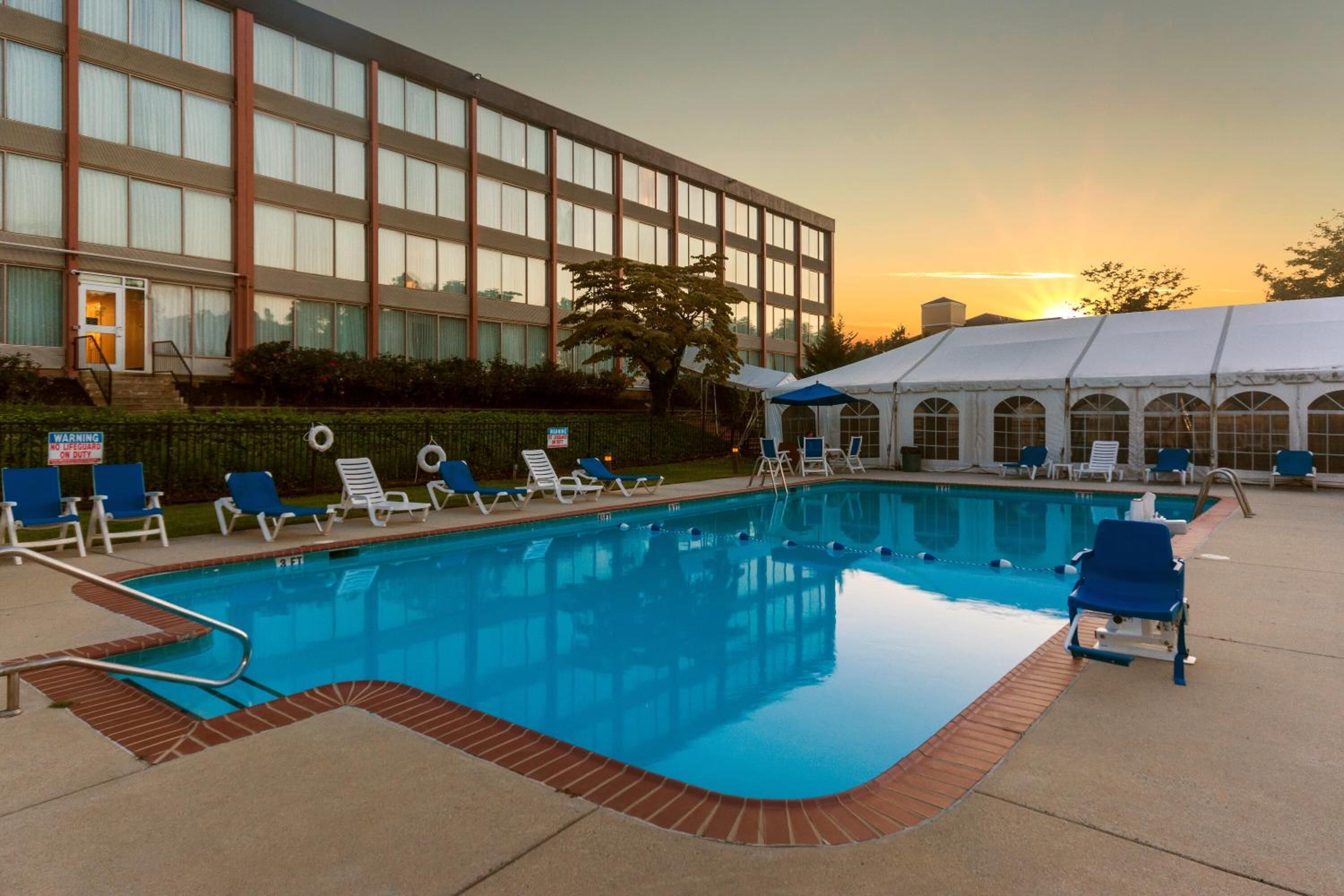 Una piscina con sillas de descanso y un área de estar techada, rodeada por un edificio con grandes ventanales.