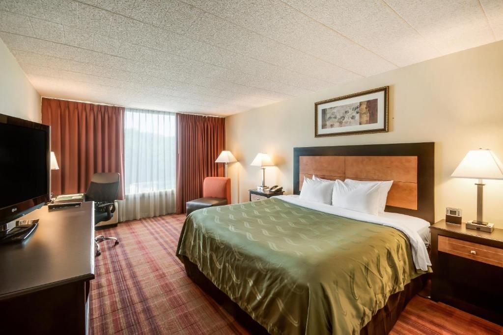 A hotel room with a bed, desk, television, and two lamps.