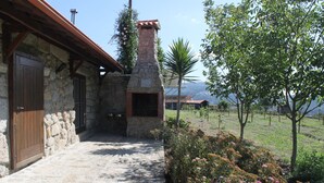 Un bâtiment en pierre doté d’une cheminée, d’une porte en bois et d’un chemin de pierre menant à un jardin agrémenté de fleurs et d’arbres.