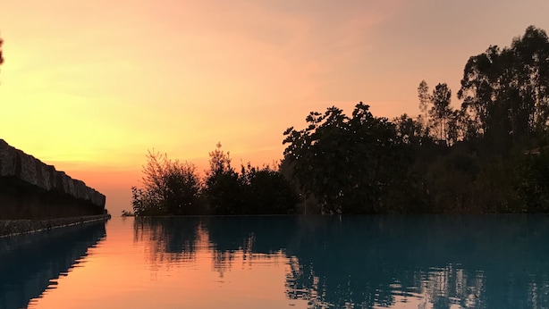 Une étendue d'eau calme où se reflète un coucher de soleil, avec des arbres et une falaise rocheuse sur un côté.