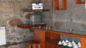 Une cuisine rustique avec un mur en pierre, un comptoir de bar en bois, des tabourets et un téléviseur fixé au-dessus du comptoir.