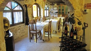 Un comedor rústico con paredes de piedra, mesas y sillas de madera. Se exhiben botellas de vino en una estantería.
