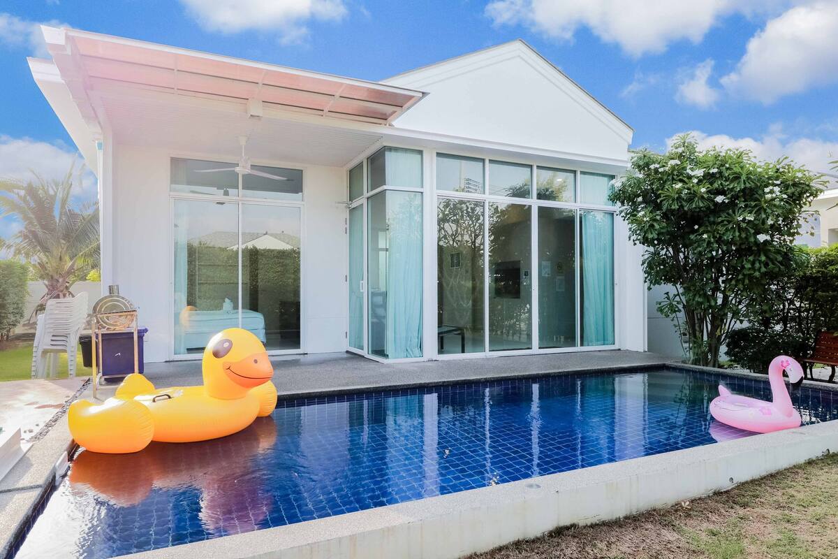 Una casa moderna con piscina, que incluye un pato y un cisne flotantes.