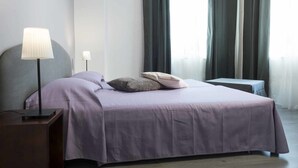 A neatly made bed with a purple bedspread and pillows, a bedside lamp, and a small table with a lamp. - B&B Sleep & Zupp (Naples)