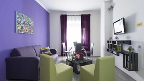 A living room with a purple wall, a sofa, two armchairs, a coffee table with flowers, a TV, and a bookshelf. - B&B Sleep & Zupp (Naples)