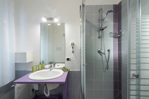 A modern bathroom with a purple vanity, a large mirror, a shower with multiple nozzles, and a glass-enclosed shower area. - B&B Sleep & Zupp (Naples)