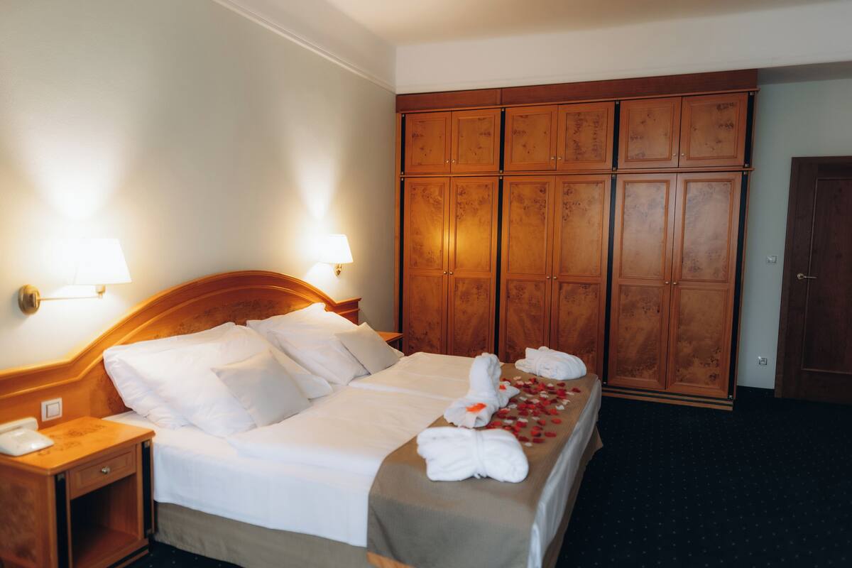 Een hotelkamer met een groot bed, een houten garderobe en bedlampjes.