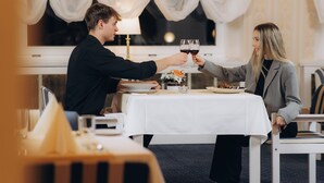 Een eetruimte met een tafel voor twee personen, een kroonluchter en een raam met dunne gordijnen.