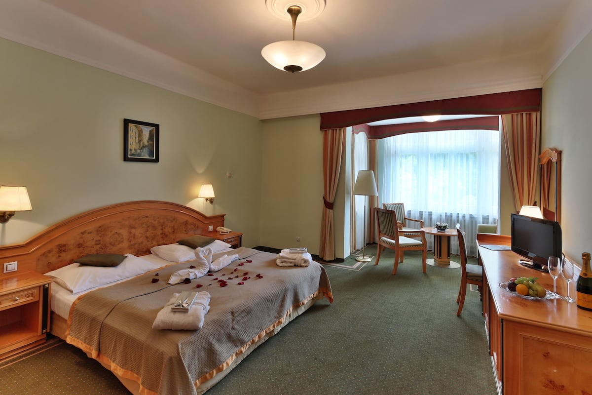 Een hotelkamer met een bed, nachtkastjes, een bureau met stoel, een televisie en een raam met gordijnen.