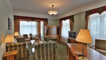 Quarto de hotel com poltronas listradas, um armário de madeira, uma televisão e uma mesa de jantar com cadeiras.