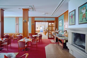 Un espace repas avec des chaises et des tables en bois, une moquette rouge et une cheminée.