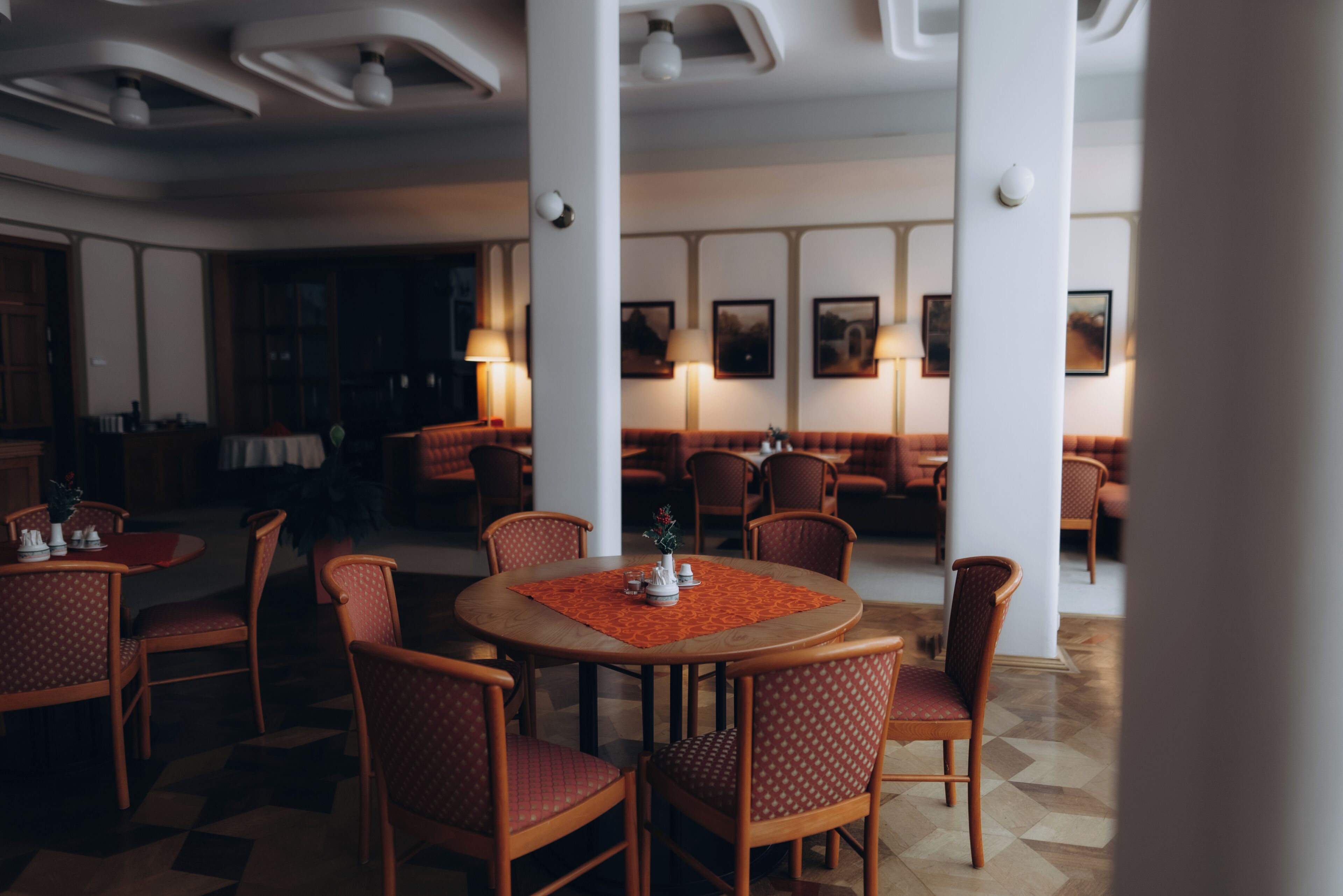 A restaurant with round tables, wooden chairs, and a patterned table runner.