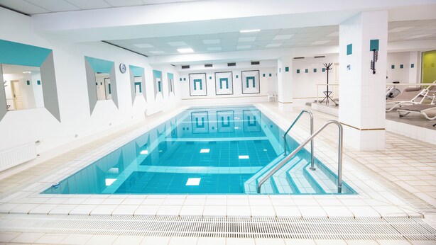 Een groot binnenzwembad met helderblauw water, omringd door witte muren en een betegelde vloer.