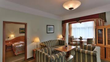 Une chambre d’hôtel comprenant un lit, un coin salon avec des fauteuils à rayures et une table, un meuble en bois et une fenêtre avec des rideaux.