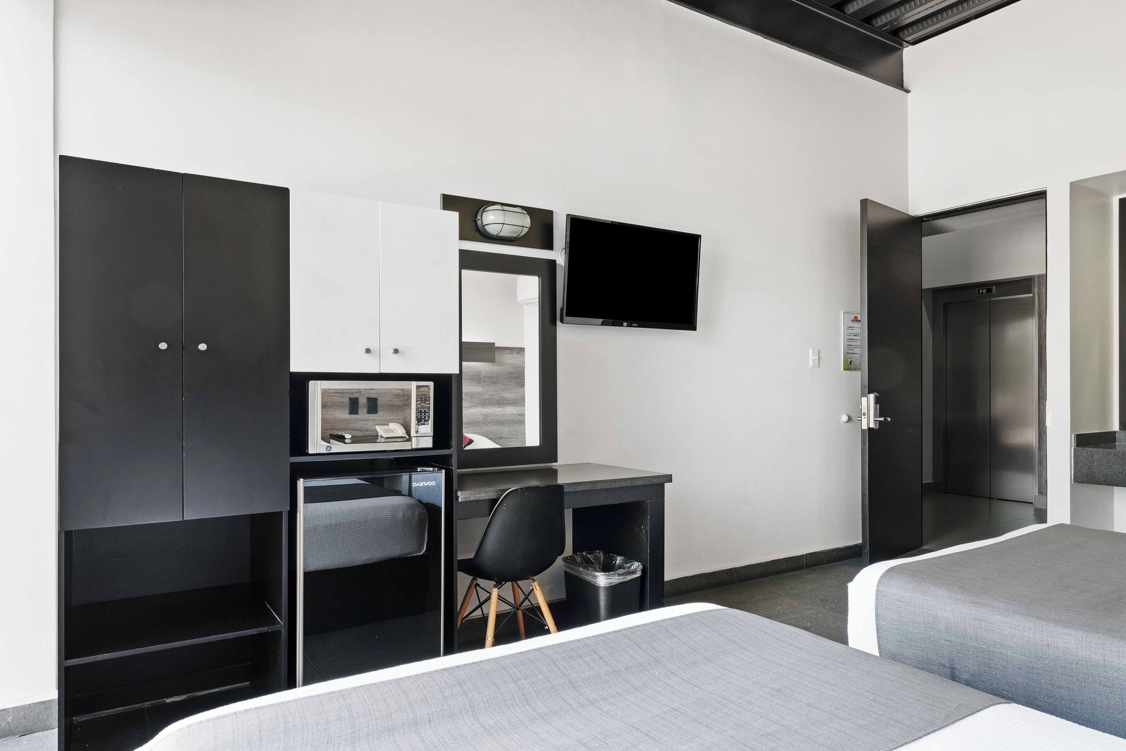 Una habitación de hotel moderna con escritorio, silla, cama y televisor montado en la pared.