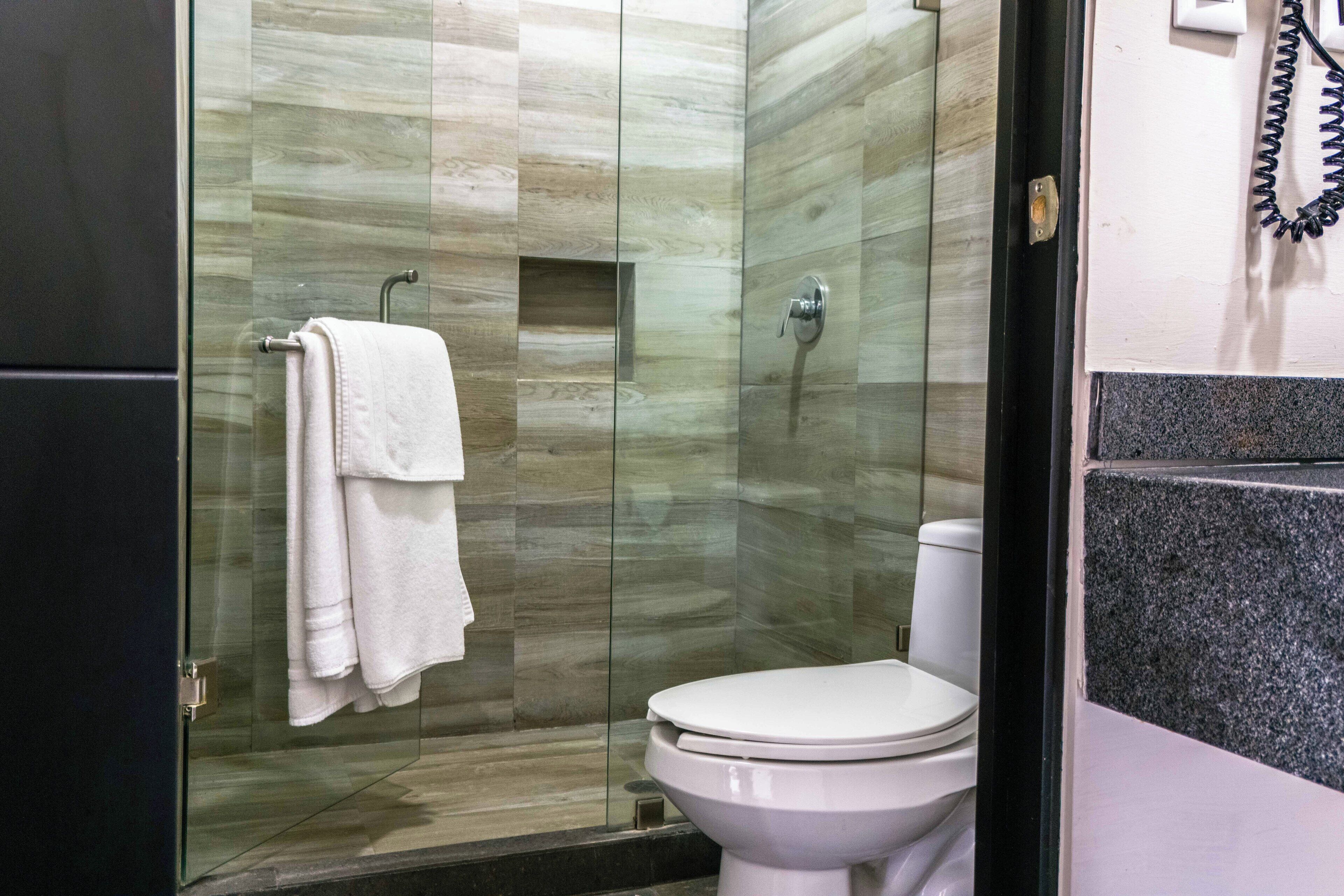 Un baño moderno con cabina de ducha de vidrio, inodoro blanco y toallero con toallas dobladas.