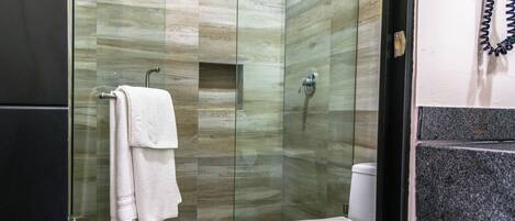 Un baño moderno con cabina de ducha de vidrio, inodoro blanco y toallero con toallas dobladas.