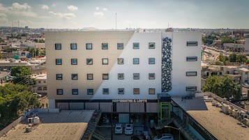 Un hotel con fachada moderna, varios pisos y un área de estacionamiento.