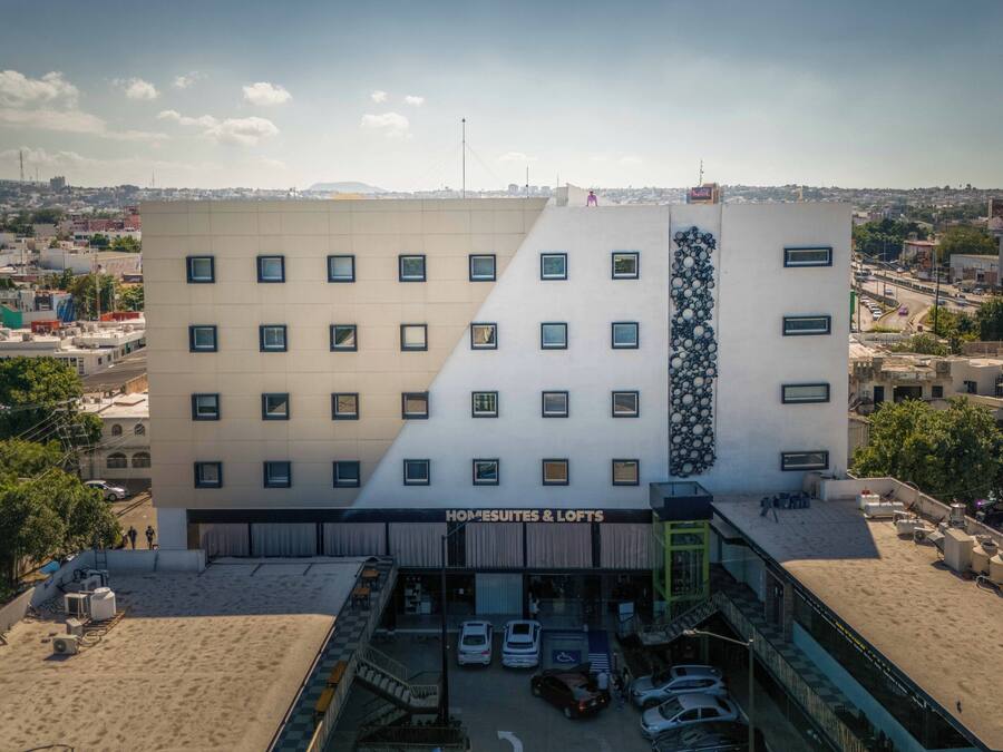 Un hotel con fachada moderna, varios pisos y un área de estacionamiento.