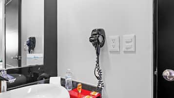 A bathroom with a white sink, a red towel rack, a hairdryer, a bottle of water, and a mirror.