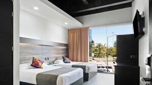 Una habitación de hotel moderna con dos camas, un ventanal amplio, un televisor de pantalla plana y una kitchenette.