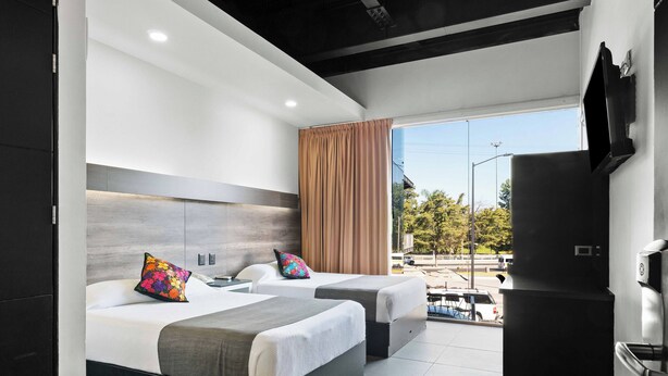 A modern hotel room with two beds, a large window, a flat-screen TV, and a kitchenette. - Homesuites Malecon (Culiacán)