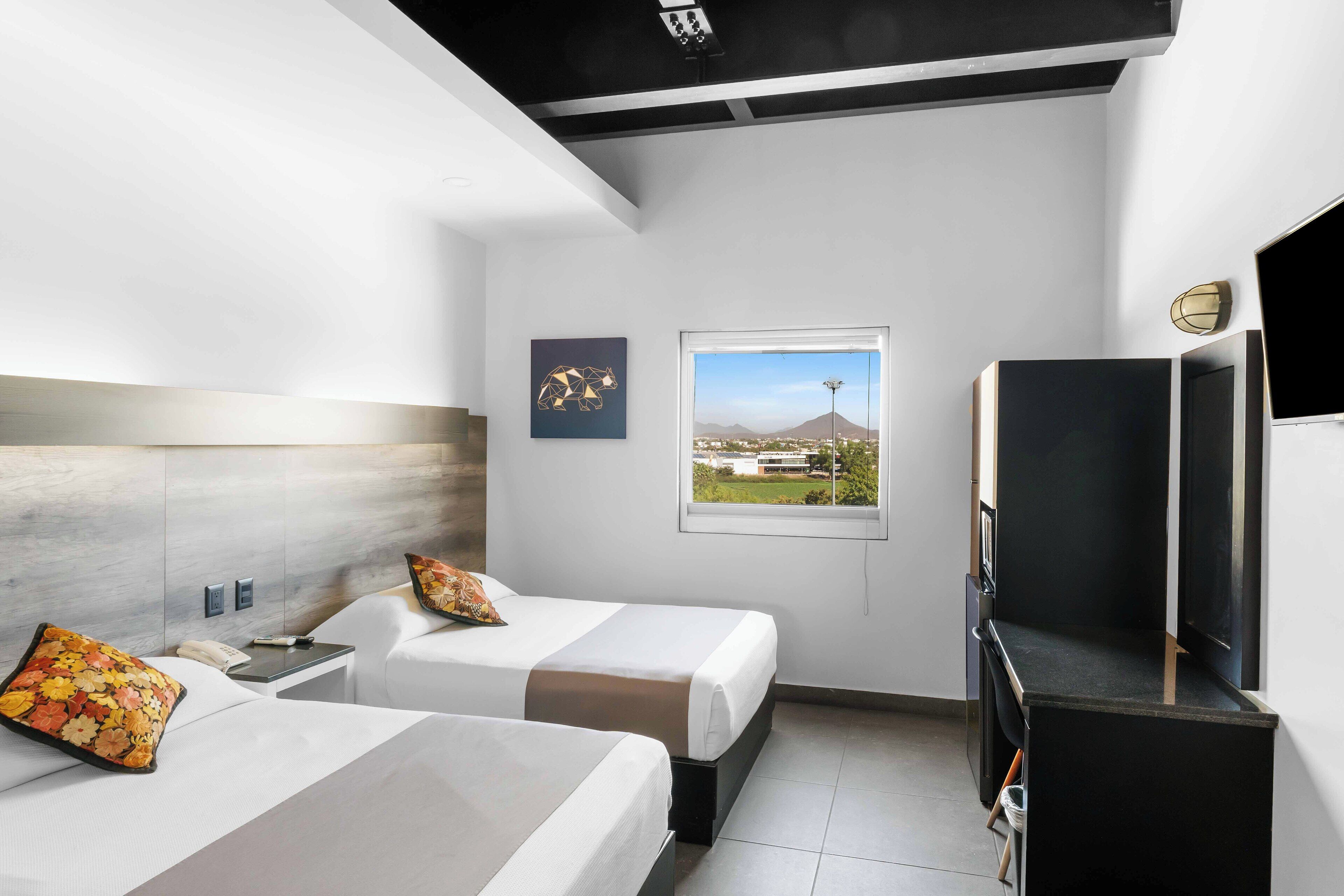 Habitación de hotel moderna con dos camas, televisión, escritorio y ventana con vistas a la ciudad.