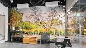 A modern interior with a mural of trees, a wooden bench, a metal chair, and a glass wall with a view of an outdoor seating area. - Homesuites Malecon (Culiacán)
