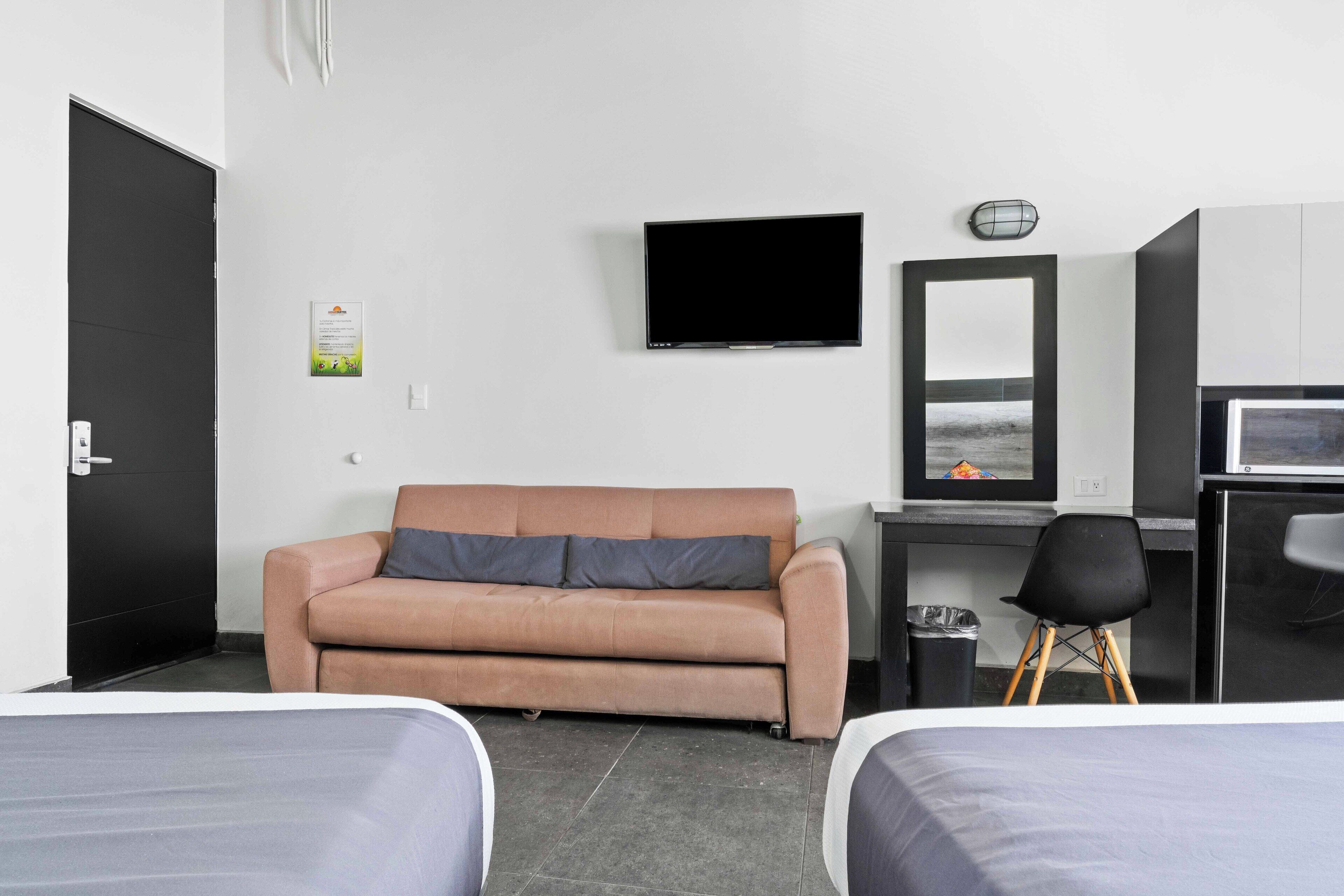 Habitación de hotel con sofá, televisión, escritorio con computadora, una silla y dos camas.