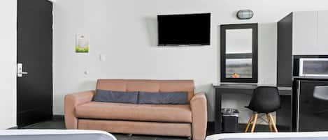 Habitación de hotel con sofá, televisión, escritorio con computadora, una silla y dos camas.