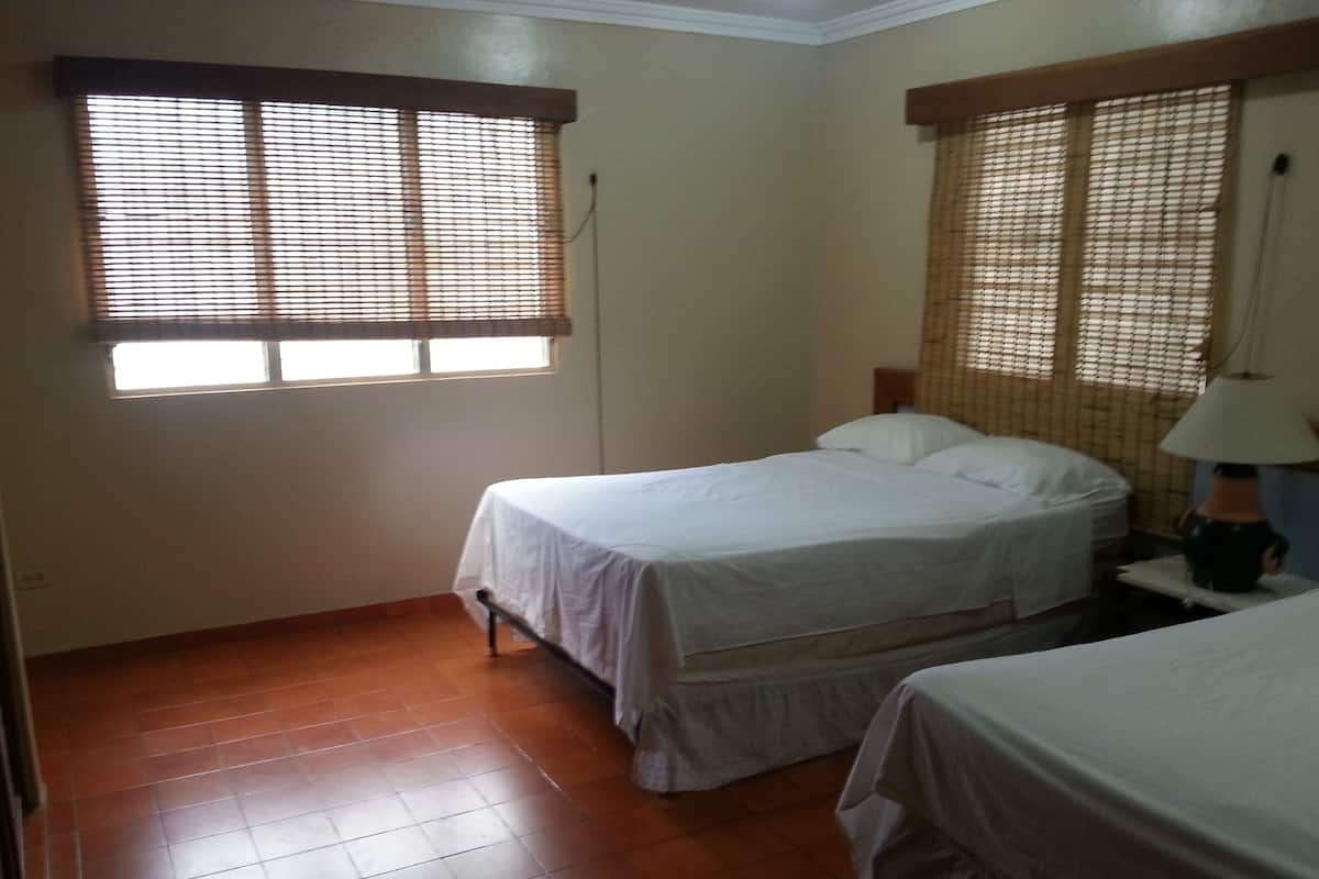 A room with two beds, a wooden floor, and windows with blinds.