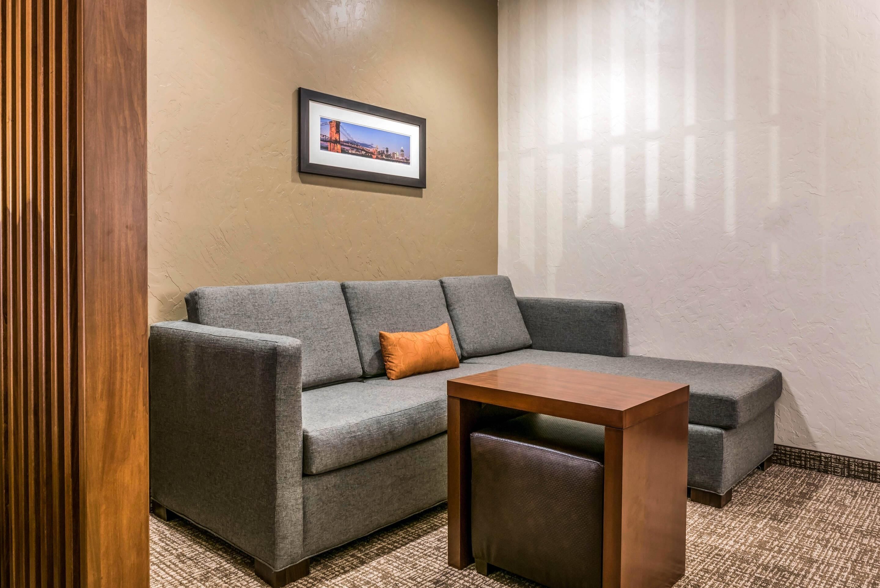 Un canapé gris avec un coussin orange, une table basse en bois et un tableau encadré accroché au mur.