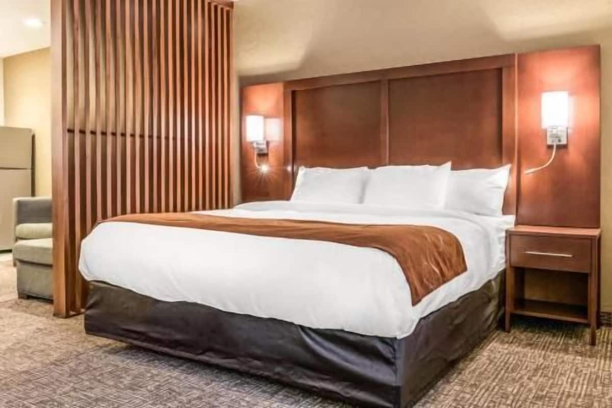 A hotel room with a large bed, wooden headboard, two bedside tables, and a wall-mounted light fixture.