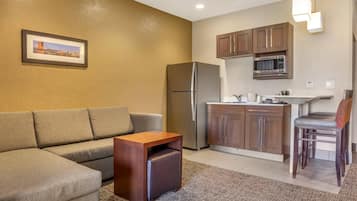 Un espacio habitable compacto con sofá, una pequeña mesa de madera, una kitchenette con microondas y refrigerador.