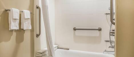 Un baño con una bañera blanca, ducha con barra de apoyo y un inodoro. Toallas colgadas en un perchero.