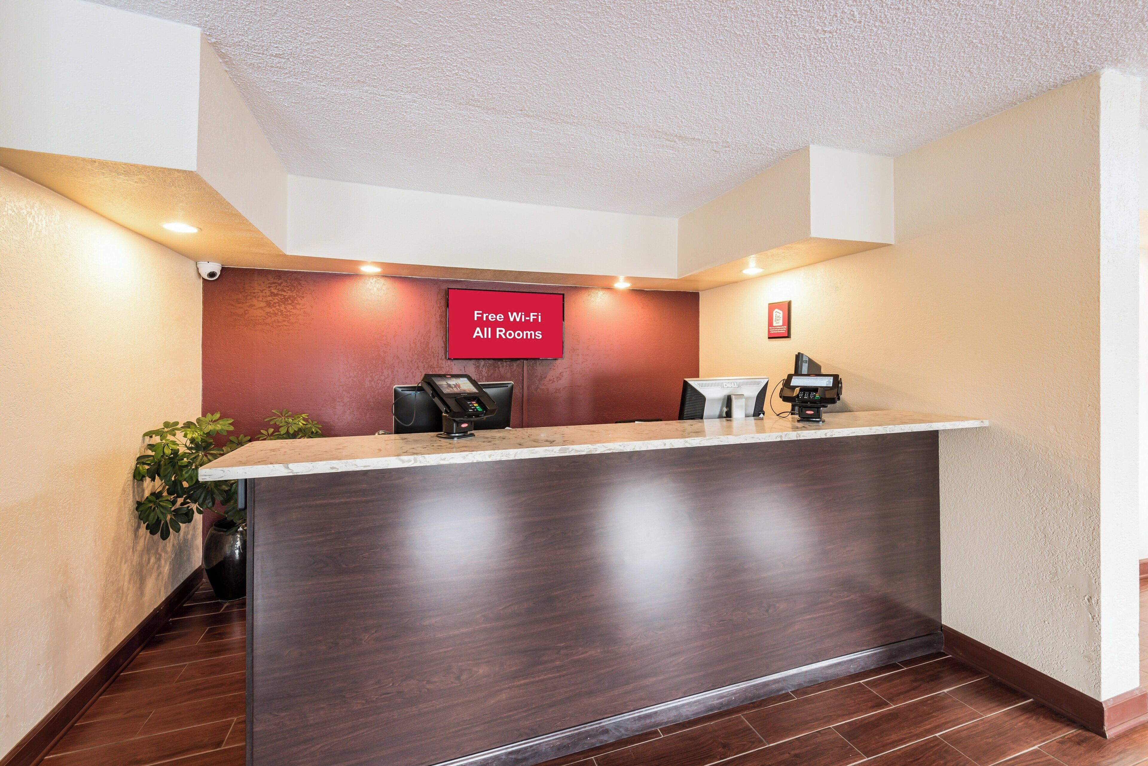 A reception desk with a digital screen, a 'Free Wi-Fi All Rooms' sign, and a security camera.