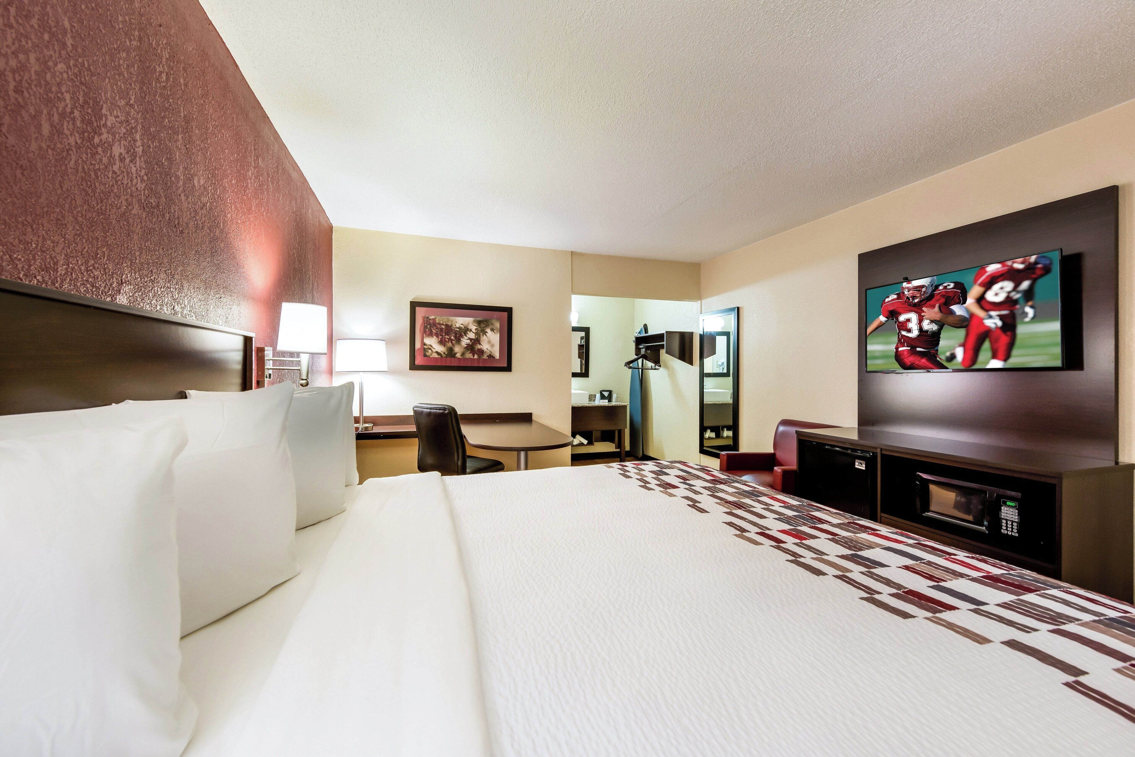 A hotel room with a large bed, a desk, a chair, a television, and a mirror.
