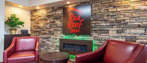 Un área de recepción con pared de piedra, letrero de Red Roof Inn, sillas de cuero, una mesita y una planta.