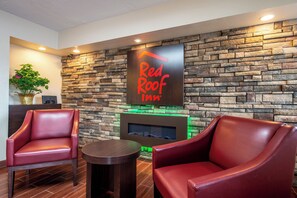 A lobby area with a stone wall, a Red Roof Inn sign, leather chairs, a small table, and a plant. - Red Roof Inn Marion, IN (Marion)