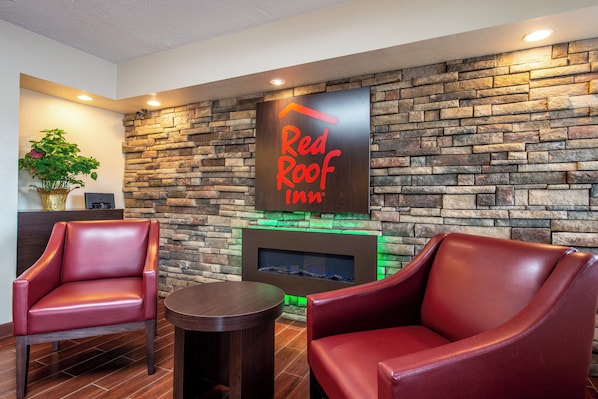 A lobby area with a stone wall, a Red Roof Inn sign, leather chairs, a small table, and a plant. - Red Roof Inn Marion, IN (Marion)