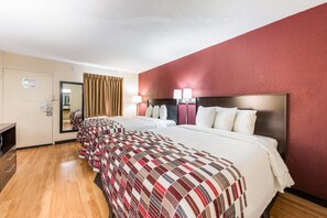 Une chambre d’hôtel avec deux lits, un plancher en bois, un mur rouge et un miroir.