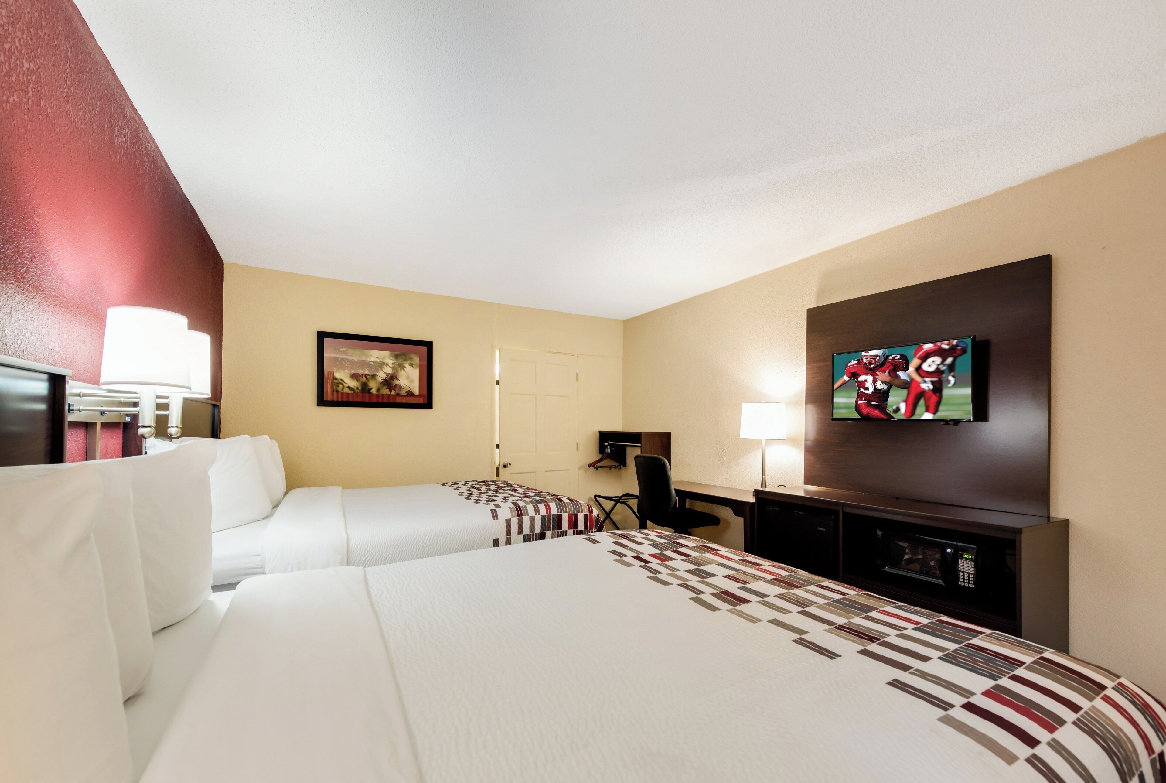A hotel room with two beds, a desk, a television, and a door.