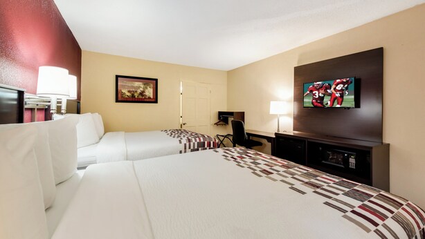 A hotel room with two beds, a desk, a television, and a door. - Red Roof Inn Marion, IN (Marion)