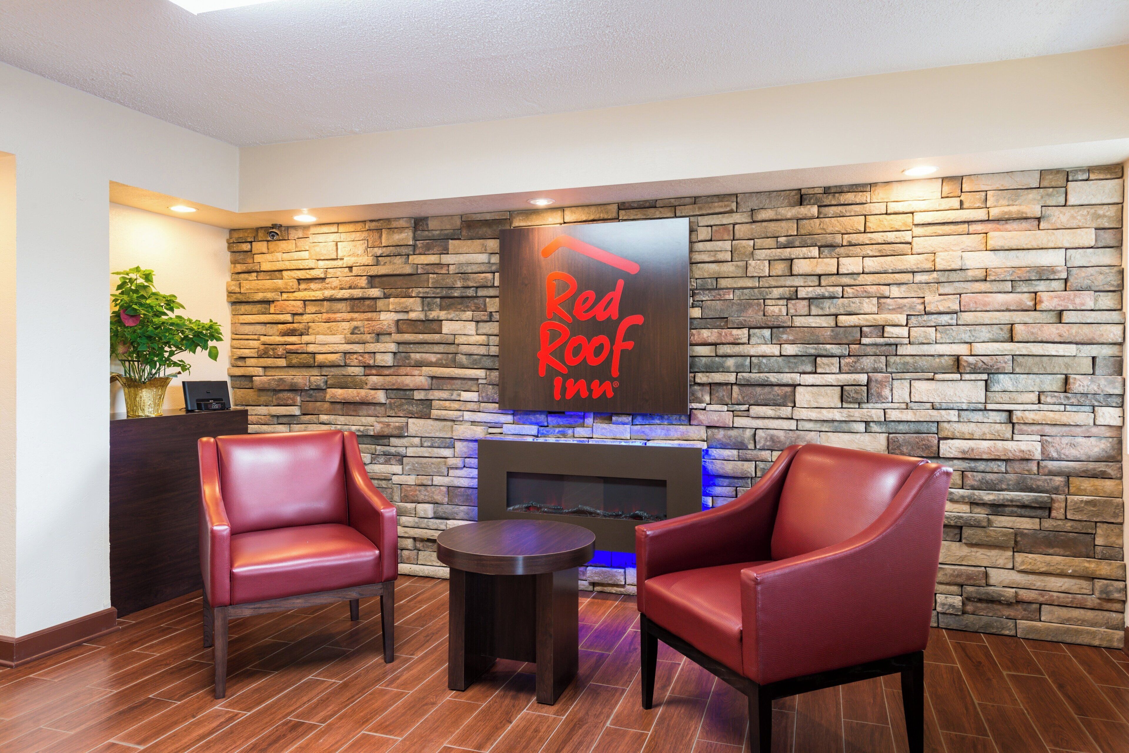 Vestíbulo de Red Roof Inn con paredes de piedra, sillones de cuero, una pequeña mesa y una chimenea.