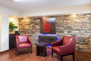 Vestíbulo de Red Roof Inn con paredes de piedra, sillones de cuero, una pequeña mesa y una chimenea.