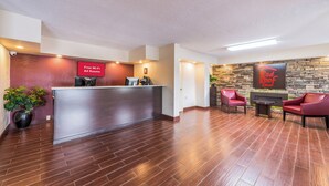 A reception area with a wooden reception desk, a potted plant, and a sign indicating free Wi-Fi. - Red Roof Inn Marion, IN (Marion)
